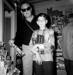 My father, John Walsh, buying me a comic book. Somewhere on our trip to the East Coast, April 1960. Ever the cinematographer, I have a movie camera around my neck. And my father looks like a Blues Brother.